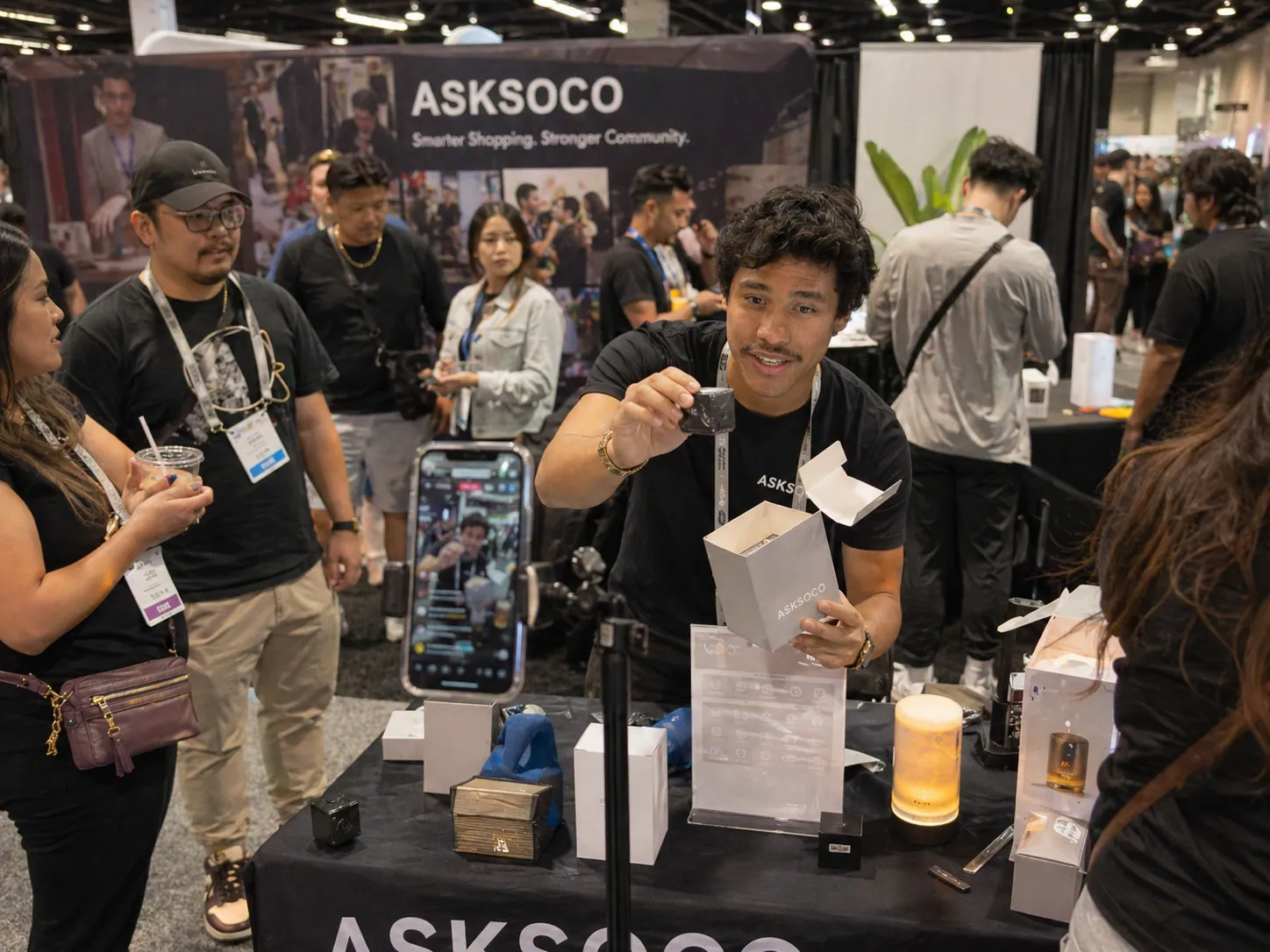 AskSoco live demo at an industry event — host presenting product on camera with audience around the booth.